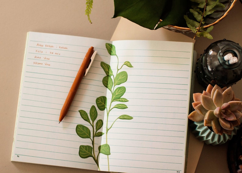 May include: An open notebook with lined pages and a brown pen. The notebook has a green leafy design on the right page. A succulent plant in a blue pot is on the right side of the notebook.