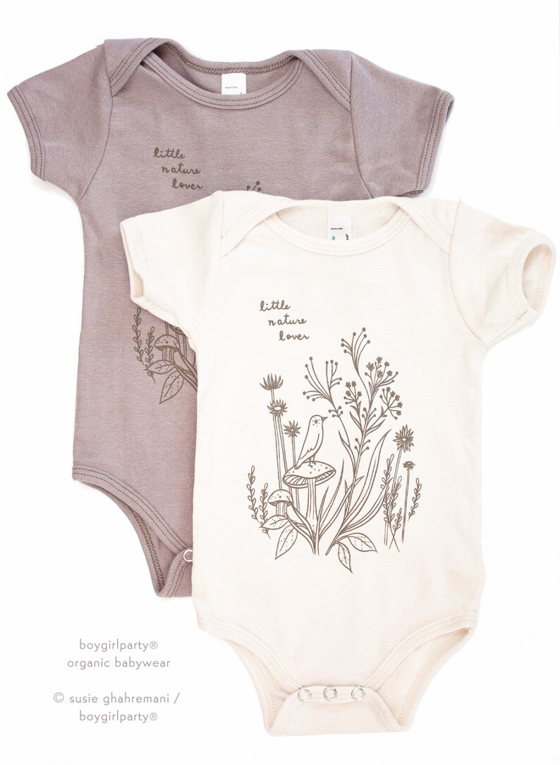 Puede incluir: Dos bodies para beb&eacute;, uno de color marr&oacute;n claro y otro de color crema. Ambos bodies tienen el texto "little nature lover" impreso en ellos. El body crema tiene un gr&aacute;fico de un p&aacute;jaro en un hongo con plantas y flores.