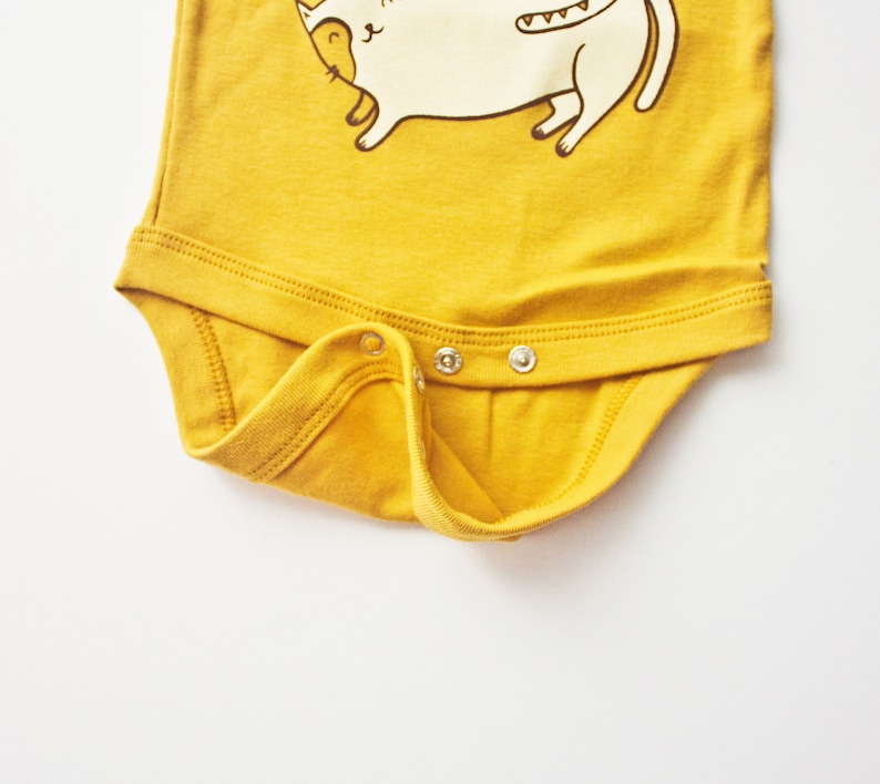 May include: A yellow baby onesie with a white cat illustration. The onesie has three snaps on the bottom.