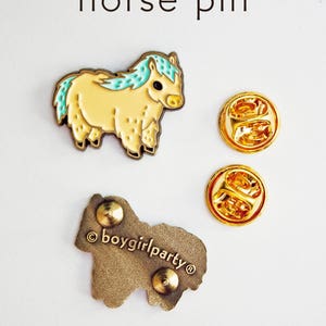 Op de afbeelding: Een gouden emaille pin met een cartoonpaard met een lichtblauwe manen en een geel lichaam. De pin is op een witte achtergrond en bevat de tekst "&copy;boygirlparty&reg;".