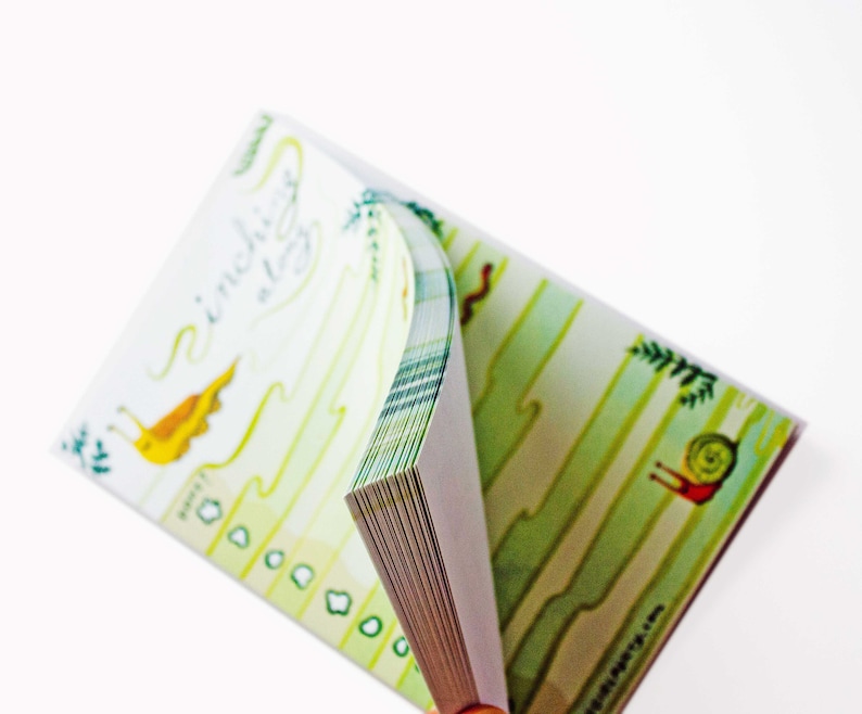 May include: A small, green and white illustrated notebook with the text "sinching along" on the cover. The notebook is open and the pages are fanned out.