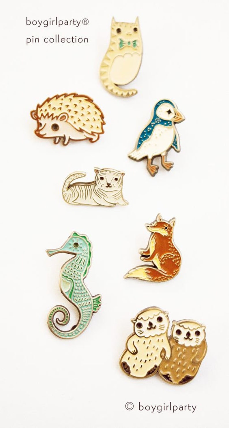 May include: A set of enamel pins featuring various animals, including a cat, hedgehog, puffin, tiger, fox, seahorse, and two otters. The pins are all in a cartoon style and have a gold finish. The text "boygirlparty&reg; pin collection" is at the top of the image.