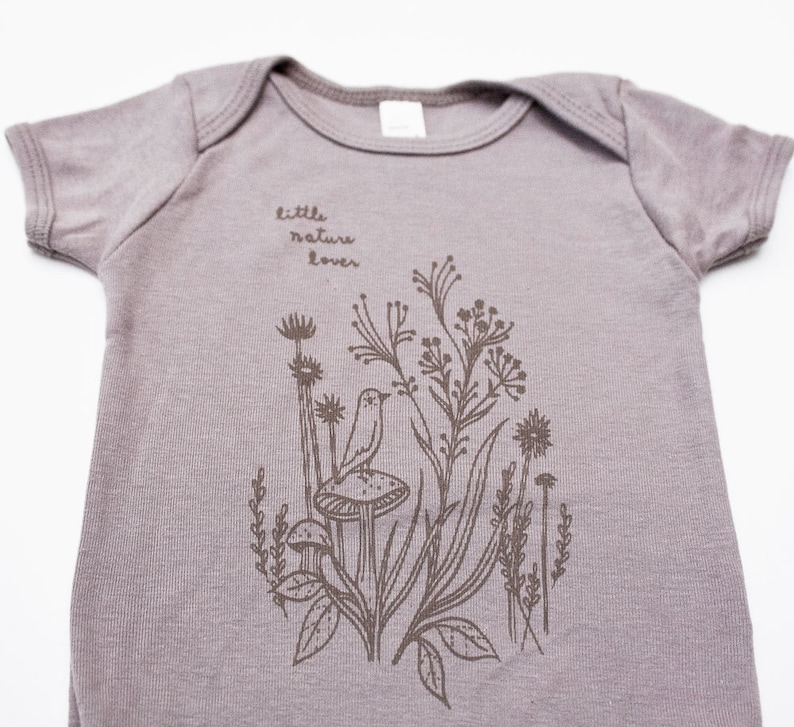 Puede incluir: Un body de beb&eacute; gris claro con un gr&aacute;fico marr&oacute;n de un p&aacute;jaro, hongos y flores. El texto "little nature lover" est&aacute; impreso en el body.