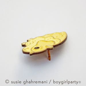 May include: A yellow enamel pin with a cartoon-style illustration of a yellow chick. The pin has a gold finish and a back pin.