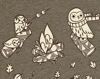 Puede incluir: Una camiseta marrón con un gráfico blanco de tres búhos alrededor de una fogata. Los búhos llevan accesorios de invierno y uno de ellos sostiene un palo con malvaviscos. El texto "boygirlparty" está impreso en la camiseta.