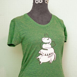 May include: Green t-shirt with a graphic of a stack of cats. The cats are white with brown outlines and are stacked on top of each other. The text "boygirlparty" is printed in brown at the top of the shirt.