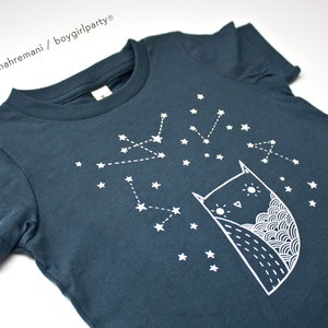 May include: A dark blue t-shirt with a white owl and constellation design. The owl is looking up at the stars. The text "susie ghahremani / boygirlparty&reg;" is in the top left corner.