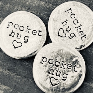 May include: Three silver pocket hug tokens with the words "pocket hug" and a heart symbol engraved on each.