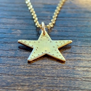 Könnte beinhalten: Eine goldene Stern-Anhänger-Kette mit einer strukturierten Oberfläche. Der Stern hängt an einer goldenen Kette.
