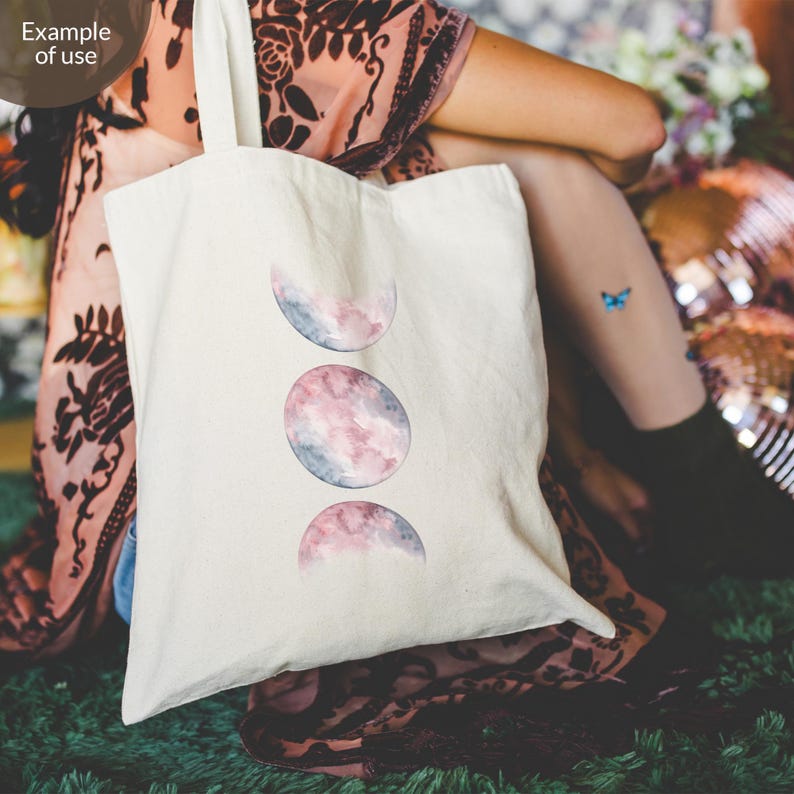 May include: A white tote bag with three watercolor moon phases in shades of pink and blue. The moon phases are stacked vertically on the bag.