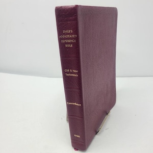 Könnte beinhalten: Ein weinrotes Hardcover-Buch mit dem Titel "Dake's Annotated Reference Bible". Der Buchrücken zeigt goldfarbene Schrift mit dem Text "Old & New Testaments" und "Concordance". Das Buch hat einen strukturierten Einband und einen goldfarbenen Buchschnitt.