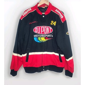 Puede incluir: Chaqueta de carreras negra, roja y blanca con la palabra "GORDON" en los hombros. La chaqueta presenta el número "24" y el logotipo "DUPONT MOTORSPORTS" en la parte delantera. La chaqueta tiene cierre de botones y cuello negro.