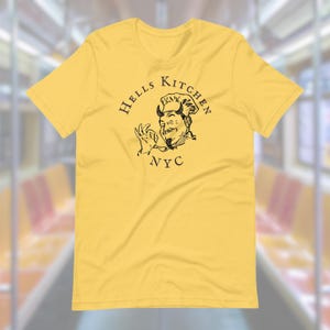 May include: Yellow t-shirt featuring a black and white illustration of a chef with horns and the text "Hells Kitchen NYC".