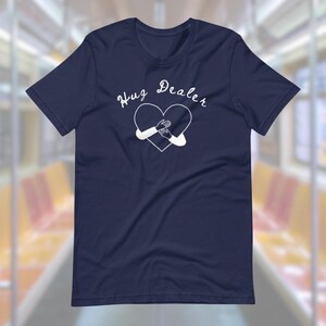 May include: A navy blue t-shirt with a white heart graphic and the text "Hug Dealer" printed on the front.