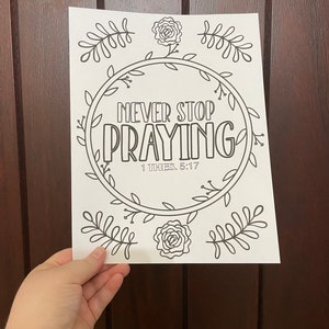 Puede incluir: Una página para colorear imprimible en blanco y negro con un diseño de corona floral. La corona rodea el texto "Never Stop Praying" con la referencia bíblica "1 THES. 5:17".