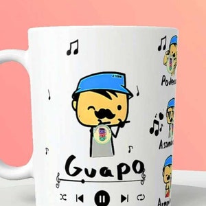 Puede incluir: Taza de cerámica blanca con un personaje de dibujos animados con bigote y gorro azul, tocando la flauta. La palabra "Guapo" está escrita debajo del personaje, junto con notas musicales y una interfaz de reproductor multimedia.