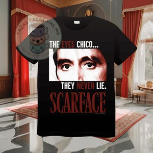 Pode incluir: Camiseta preta com um gr&aacute;fico vermelho dos olhos de Al Pacino do filme Scarface. O texto "THE EYES CHICO... THEY NEVER LIE. SCARFACE" est&aacute; impresso na camiseta.