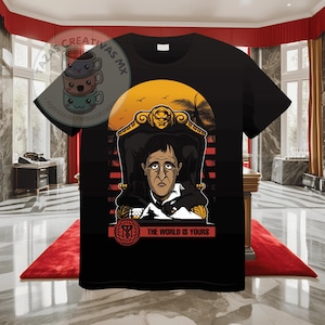 Pode incluir: Camiseta preta com um gr&aacute;fico de um homem sentado em um trono com um fundo de p&ocirc;r do sol. O texto "The World Is Yours" &eacute; impresso abaixo da imagem.