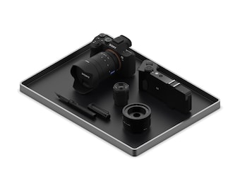 Puede incluir: Una bandeja negra con borde plateado contiene una cámara Sony con una lente, una lente pequeña, una cámara, un bolígrafo y una tapa de lente. La lente de la cámara tiene un anillo rojo.