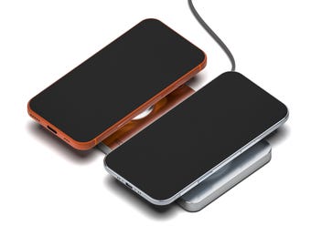 Puede incluir: Se muestran dos teléfonos inteligentes con pantallas negras. Un teléfono tiene una carcasa naranja y está colocado en un cargador inalámbrico. El otro teléfono tiene una carcasa plateada y también está en un cargador inalámbrico. Un cable negro está conectado al cargador.
