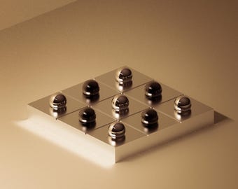 Puede incluir: Composición geométrica con una cuadrícula cuadrada con esferas negras y plateadas alternas. Las esferas están dispuestas en un patrón de 3x3 sobre una superficie metálica, creando una estética moderna y minimalista.