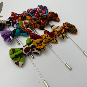 Könnte beinhalten: Ein Set aus zehn bunten Fliegennadeln mit verschiedenen afrikanischen Druckstoffen. Die Nadeln sind silberfarben und haben ein langes, dünnes Design.