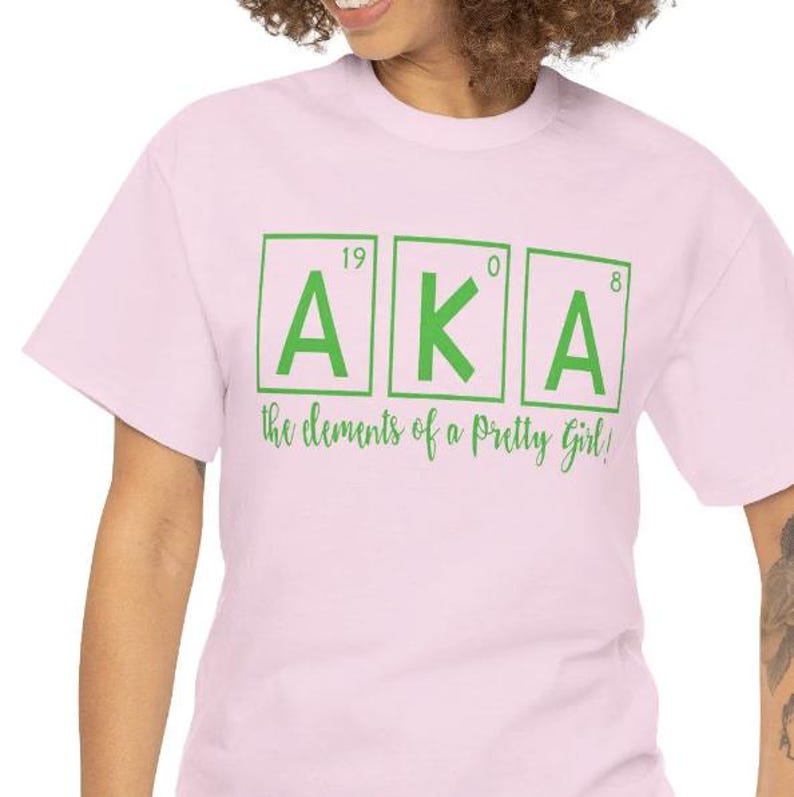 May include: Pink t-shirt with a green graphic of the letters AKA in boxes with numbers above them. The text "the elements of a pretty girl!" is below the letters.