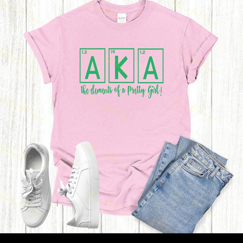 May include: Pink t-shirt with a green graphic of the letters "AKA" in a periodic table style. The text below reads "the elements of a pretty girl!"