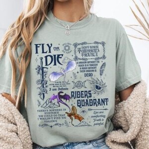 May include: A light green t-shirt with a graphic print of dragons and the text "Fly or Die", "Don't  Show  Me  Your  Horoscope  I'm  A  Wizard", "A  Dragon  Without  Its  Rider  Is  A  Tragedy  In  Search  Of  A  Story  Their  Shadow  Is  Dead", "Riders Quadrant", and "Lies  Are  Comforting  Truth  Is  Painful".