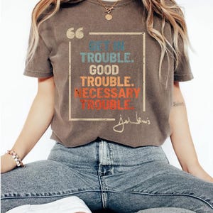 May include: A brown t-shirt with a vintage-style graphic that says "Get in Trouble. Good Trouble. Necessary Trouble." with a signature below the text.