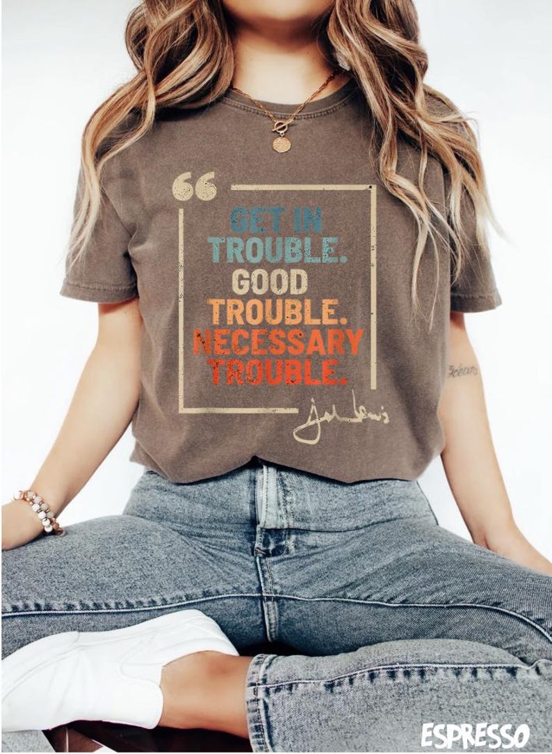 May include: A brown t-shirt with a vintage-style graphic that says "Get in Trouble. Good Trouble. Necessary Trouble." with a signature below the text.
