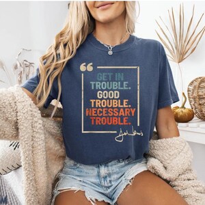 May include: A navy blue t-shirt with a vintage-style graphic that reads "Get in Trouble. Good Trouble. Necessary Trouble." with a signature below the text.
