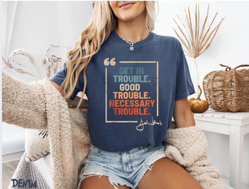 May include: A navy blue t-shirt with a vintage-style graphic that reads "Get in Trouble. Good Trouble. Necessary Trouble." with a signature below the text.