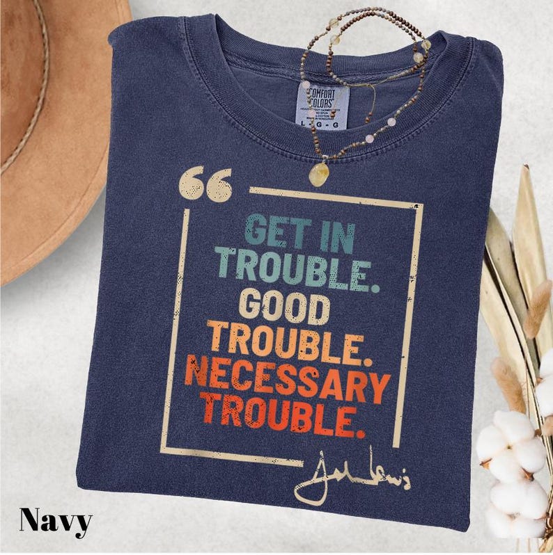 May include: Navy blue t-shirt with a vintage-style graphic that reads "Get in Trouble. Good Trouble. Necessary Trouble." and a signature that says "John Lewis".