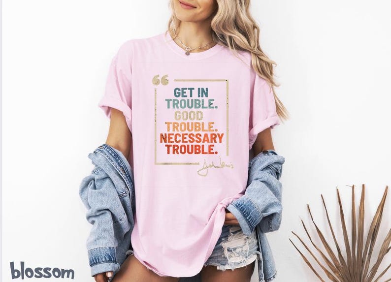 May include: Pink t-shirt with a graphic print that says "Get in Trouble. Good Trouble. Necessary Trouble." with a signature underneath.