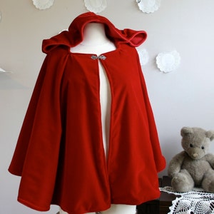 May include: A red velvet hooded cape with a silver clasp. The cape is lined with a red fabric and has a long, flowing design.