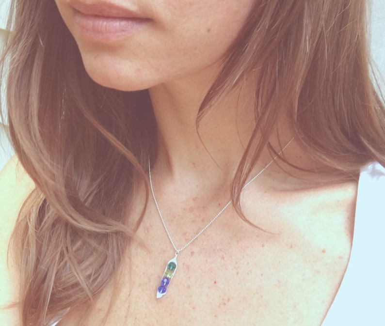 May include: A silver chain necklace with a pendant shaped like a pea pod. The pea pod is made of green, blue, and purple enamel.