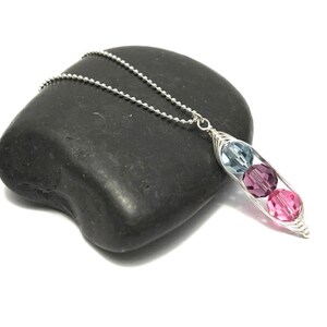 May include: A silver necklace with a pea pod charm featuring three crystal beads in shades of blue and pink.