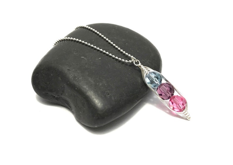 May include: A silver necklace with a pea pod charm featuring three crystal beads in shades of blue and pink.