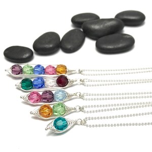 May include: Five silver necklaces with a pea pod charm featuring three colorful crystal beads. Each necklace has a different color combination of beads.
