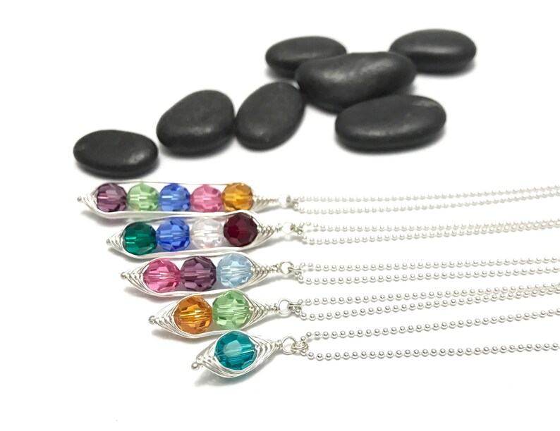 May include: Five silver necklaces with a pea pod charm featuring three colorful crystal beads. Each necklace has a different color combination of beads.