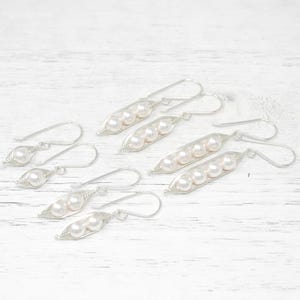 May include: A set of six silver earrings shaped like pea pods with pearl beads inside. Each earring has a silver hook.