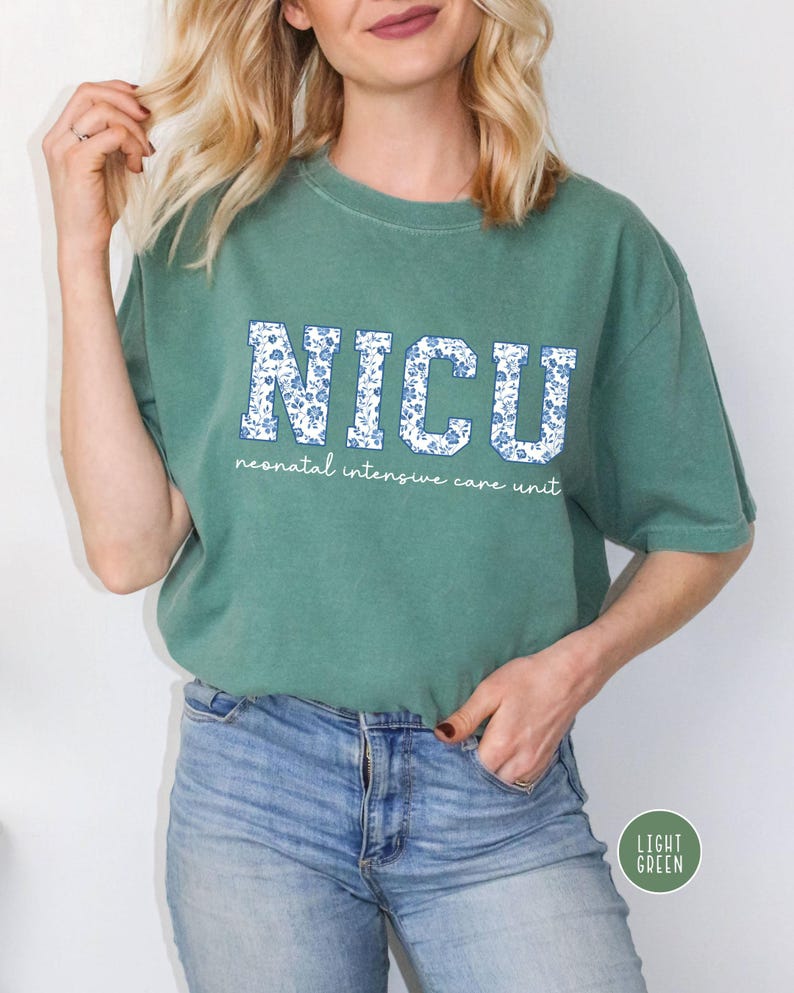 May include: A light green t-shirt with a white floral print that says "NICU" in large letters. The text below the letters says "neonatal intensive care unit".