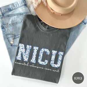 May include: A gray t-shirt with a white floral design that spells out "NICU" and the text "neonatal intensive care unit".
