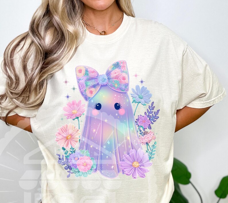 Pode incluir: Camiseta creme com um design de fantasma fofo. O fantasma &eacute; adornado com um la&ccedil;o floral e cercado por flores em tons pastel. O design tem um esquema de cores do arco-&iacute;ris, com tons de rosa, roxo e azul. A camisa &eacute; um estilo casual e confort&aacute;vel.