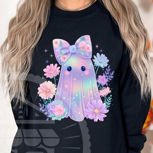 Pode incluir: Camisola preta com um design de fantasma fofo com um la&ccedil;o floral e rodeado por flores. O fantasma tem um esquema de cores arco-&iacute;ris pastel. O design inclui estrelas e um rosto fofo.