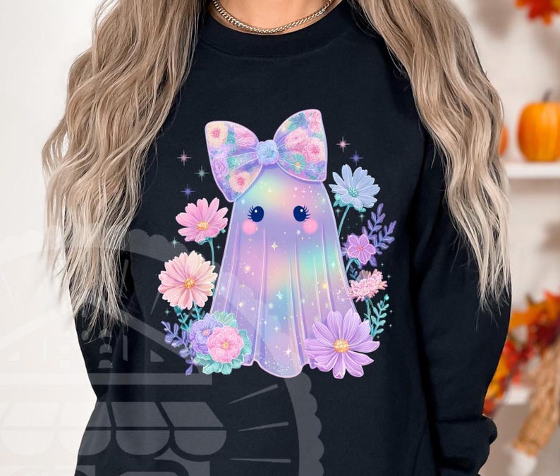 Pode incluir: Camisola preta com um design de fantasma fofo com um la&ccedil;o floral e rodeado por flores. O fantasma tem um esquema de cores arco-&iacute;ris pastel. O design inclui estrelas e um rosto fofo.