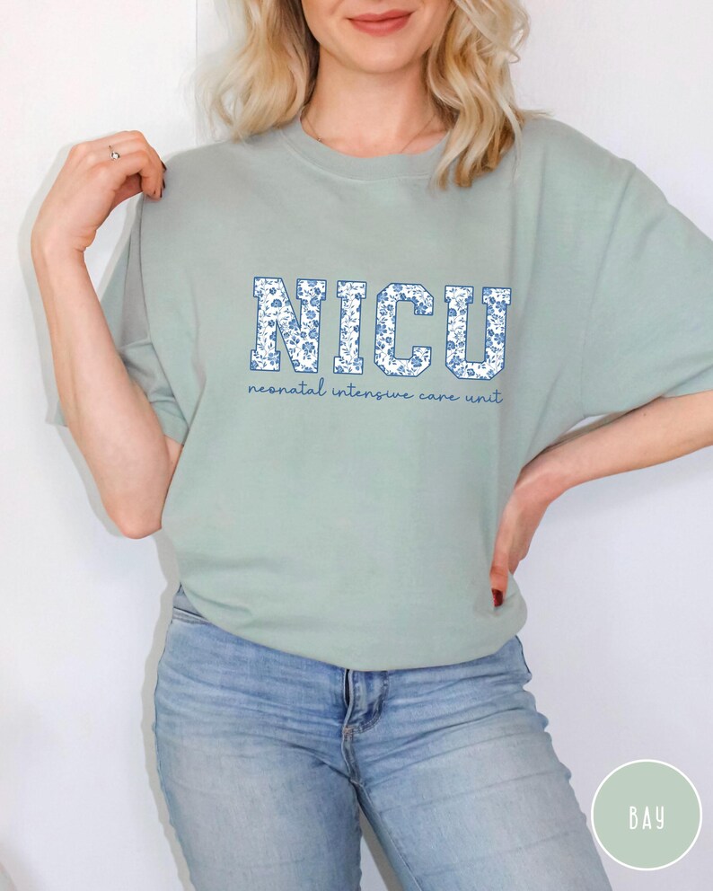 May include: A light green t-shirt with a floral print design that spells out "NICU" in large letters. The text below the letters reads "neonatal intensive care unit".