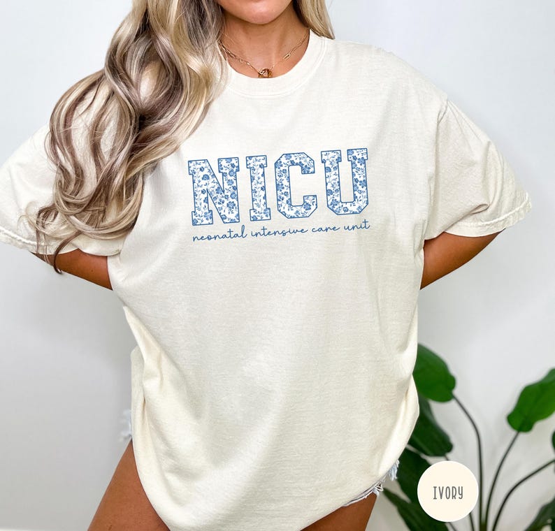 May include: A white t-shirt with a blue floral pattern spelling out "NICU" and the text "neonatal intensive care unit" below. The shirt is available in ivory.