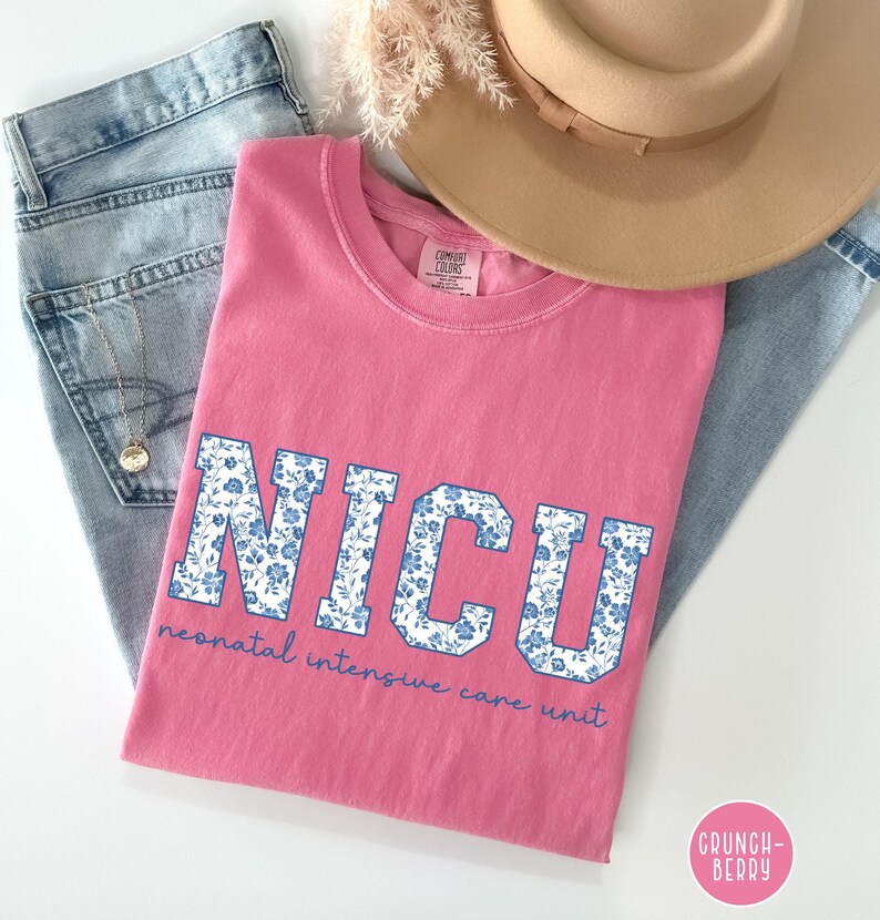 May include: Pink t-shirt with a blue and white floral print of the word "NICU" and the text "neonatal intensive care unit" in white.